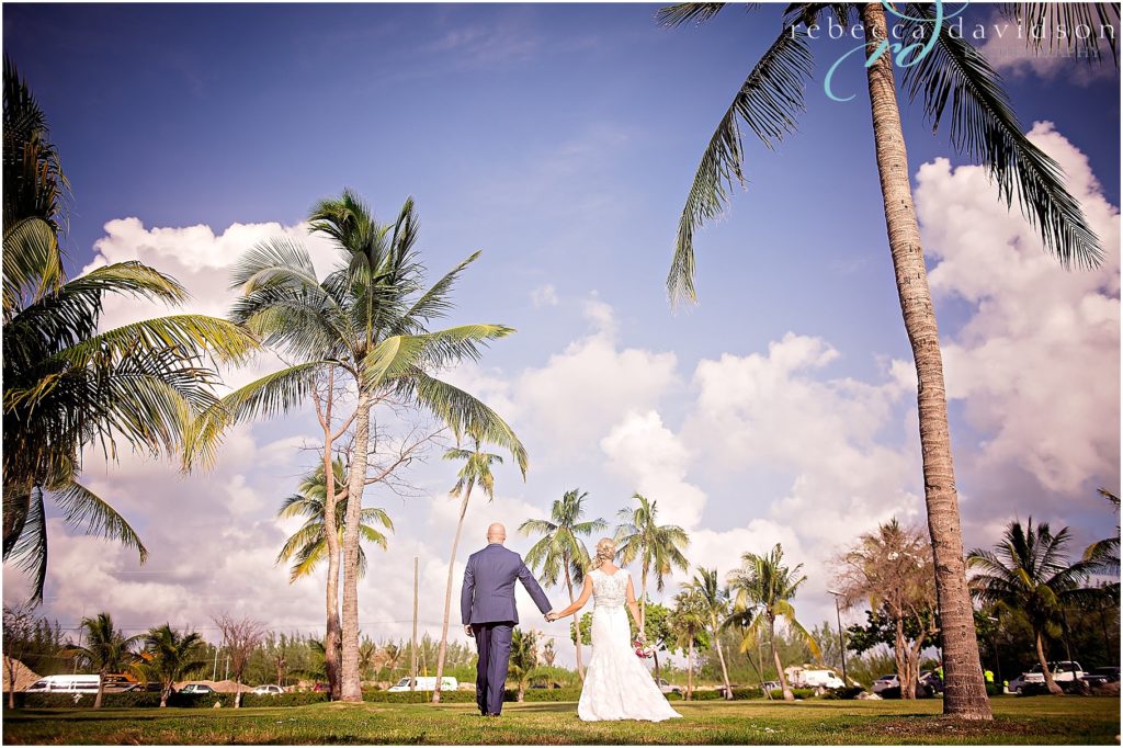 bride and groom in navy walking among coconut trees